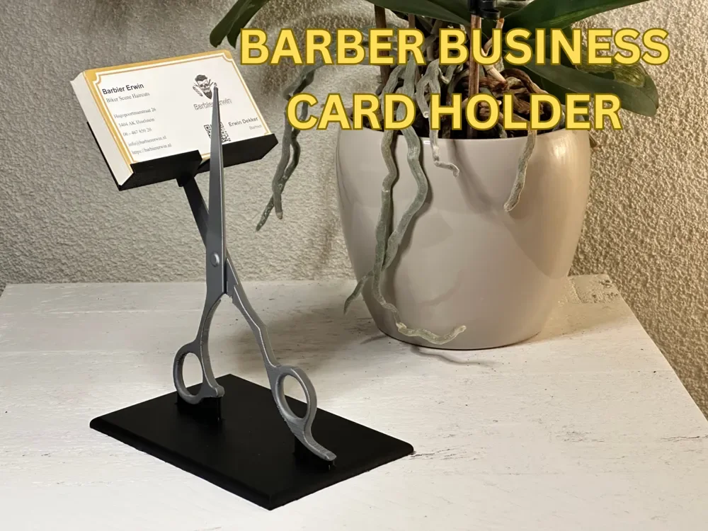 Visittkortholder for frisør og barberer med sølvgrå saksfigur, sort kortstøtte og rektangulær sort fot med visittkort øverst.