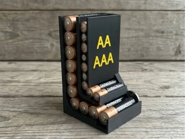 Mørk stående batteriholder fylt med AA- og AAA-batterier, med åpne sidespor, trinnvis front og tydelig gul AA/AAA-merking.