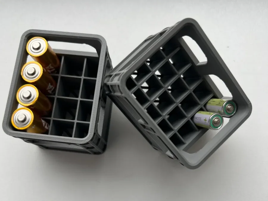 Mørkegrå, stabelbare batteriholdere formet som små bruskasser, med åpent rutemønster og flere batterier plassert i rommene.