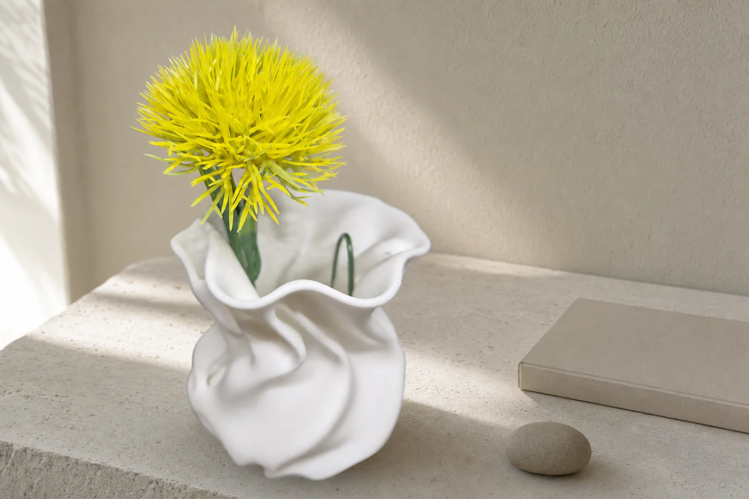 Liten lys vase med avrundet kropp, organiske folder og bølgende åpning, vist med en gul blomst mot mørk bakgrunn.