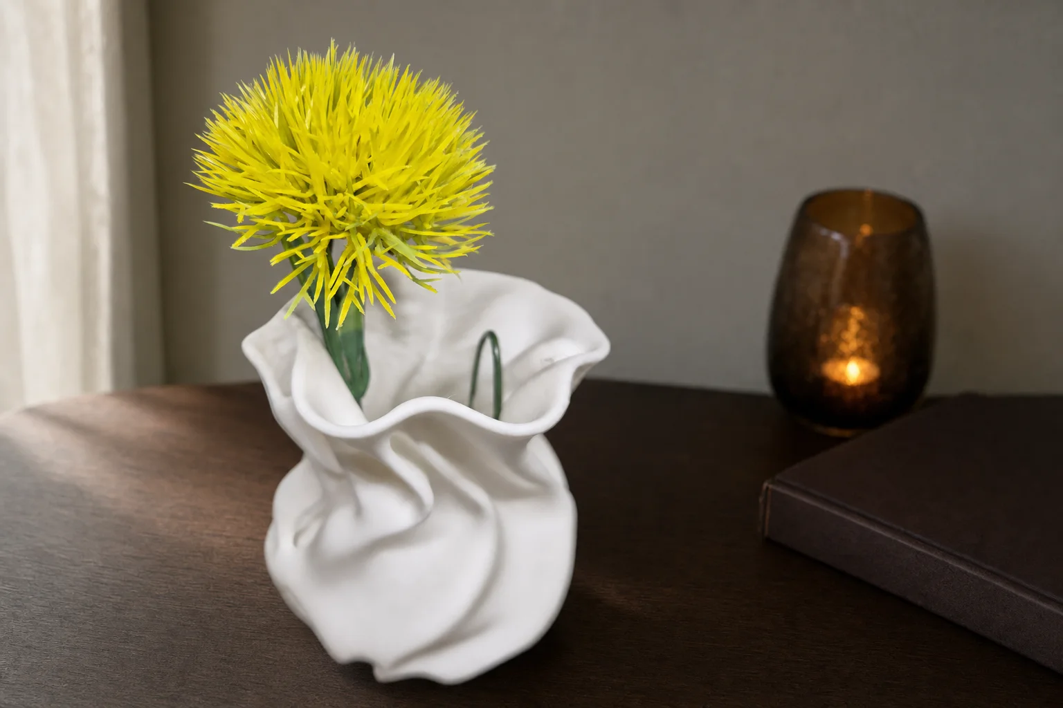 Liten lys vase med avrundet kropp, organiske folder og bølgende åpning, vist med en gul blomst mot mørk bakgrunn.