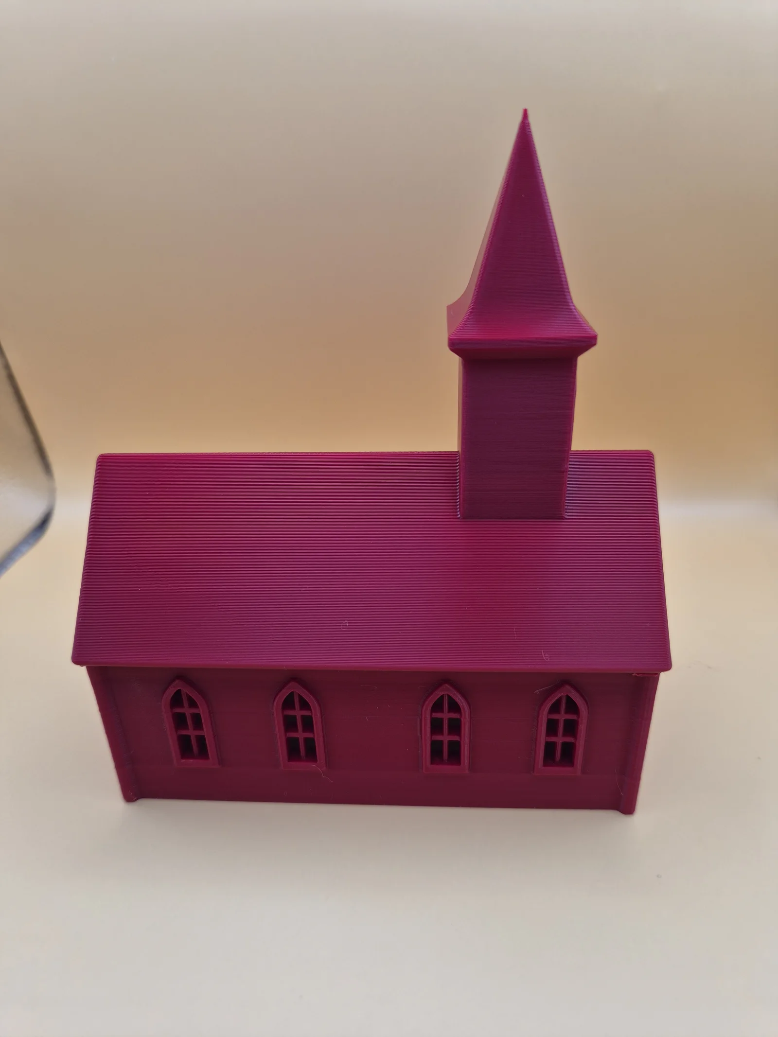 Rød dekorativ kirke med saltak, fire spissbuede vinduer og høyt tårn med spisst spir.
