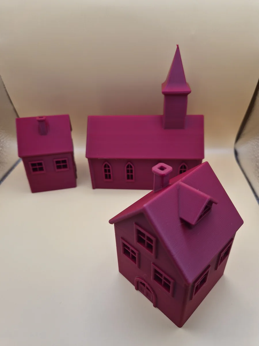 Tre rosa–magenta julebybygninger med en kirke og to ulike hus, fotografert på lys bakgrunn.