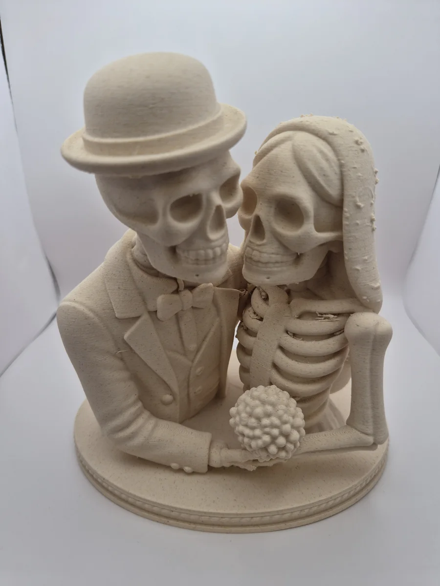 Lys beige Halloween-dekorasjon av et skjelettbrudepar med hatt, slør og bukett på rund sokkel.