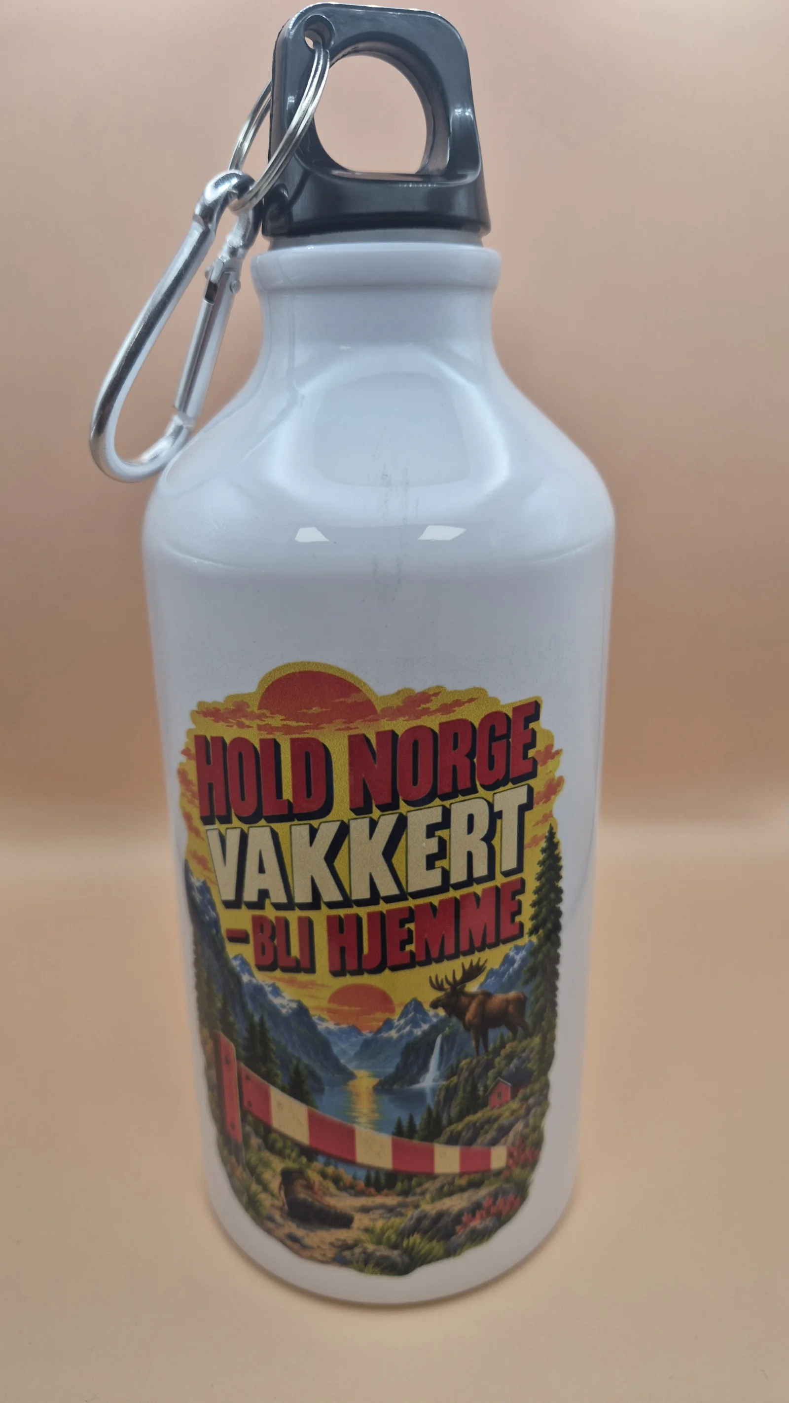 Hvit drikkeflaske med svart topp, bærehåndtak og metallfarget karabinkrok, dekorert med tekst og et fargerikt norsk naturmotiv med fjell, skog, vann, elg og veibom.